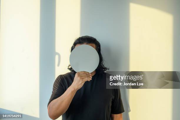 man holding mirror in front of his face at a wall - marcio foto e immagini stock