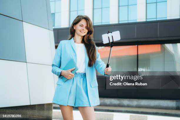 young woman taking selfie on mobile phone in stick outdoors. - selfie stick stock pictures, royalty-free photos & images