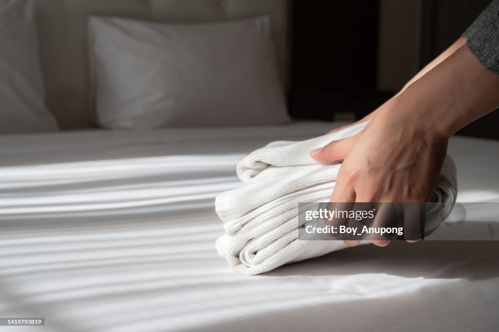 Close up of hotel maid hands arranging the stack of towels on bed in hotel bedroom.