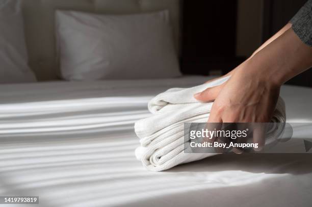 close up of hotel maid hands arranging the stack of towels on bed in hotel bedroom. - towel stockfoto's en -beelden