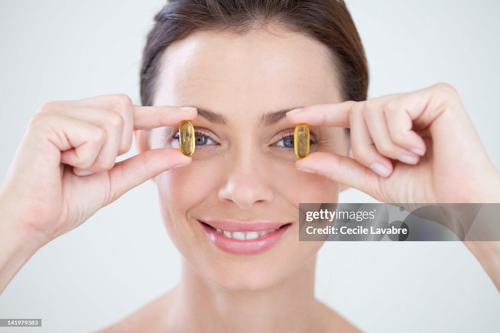 Woman holding oil capsules in front of eyes