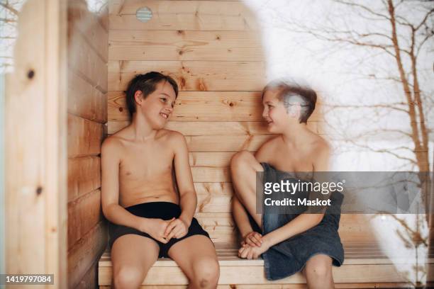 smiling shirtless boys talking with each other while sitting in sauna - young boy in sauna stock pictures, royalty-free photos & images