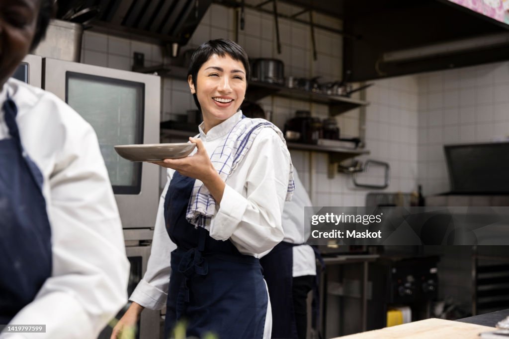 Smiling chef carrying plate while walking in restaurant kitchen