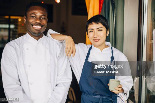 portrait of smiling multiracial chefs standing at entrance of restaurant - catering black uniform stockfoto's en -beelden