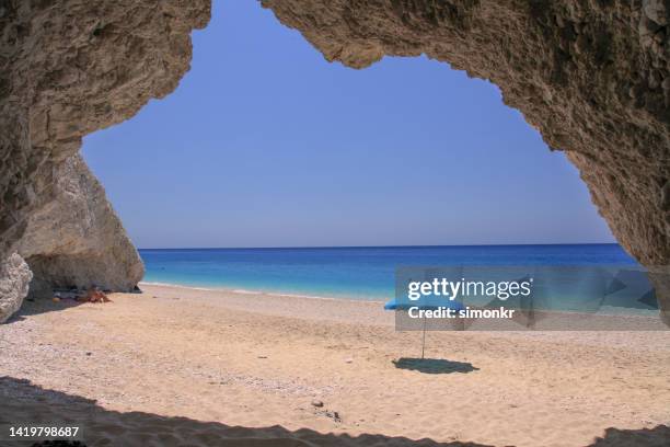 view of cave and umbrella on egremni beach - egremni beach stock pictures, royalty-free photos & images