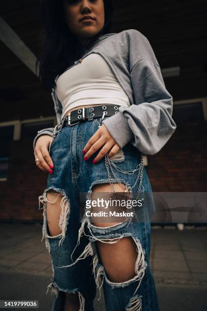 midsection of young woman in torn jeans standing on footpath - zerrissene jeans stock-fotos und bilder
