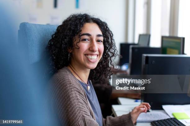 side view of happy businesswoman sitting at desk in office - incidental people stock pictures, royalty-free photos & images