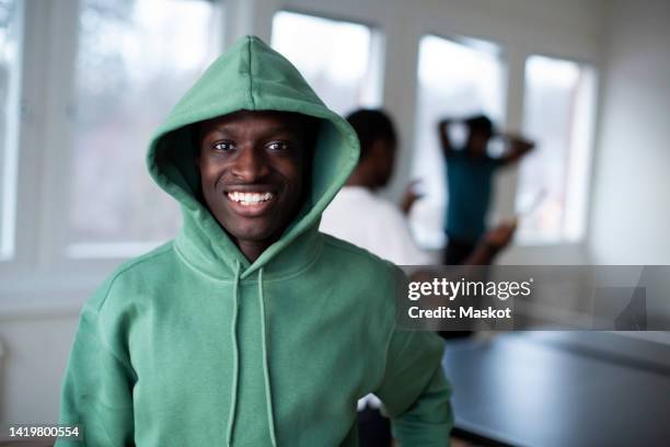 portrait of smiling teenage boy in green hooded shirt standing in games room - boy clothes stockfoto's en -beelden