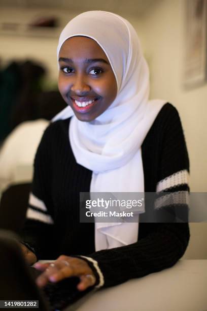 portrait of smiling girl sitting with laptop in classroom - hijab girl stock-fotos und bilder