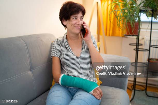 frau mit gebrochenem arm beim telefonieren - knochenbruch stock-fotos und bilder