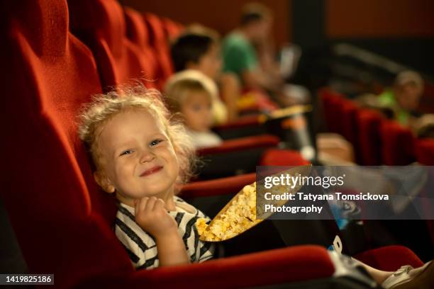 cute child, curly girl, watching movie in a cinema, eating popcorn and enjoying - filmindustrie stockfoto's en -beelden