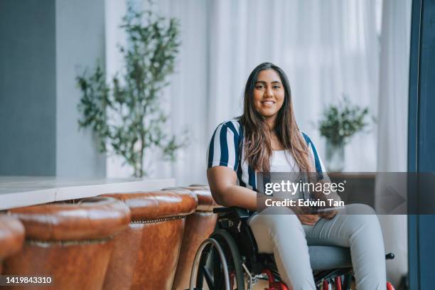 asian indian woman with disabilities sitting on wheelchair looking at camera smiling in meeting room - rolstoel stockfoto's en -beelden