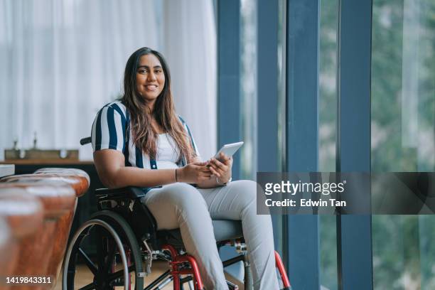 asian indian woman with disabilities sitting on wheelchair looking at camera smiling in meeting room - disabled accessibility stock pictures, royalty-free photos & images