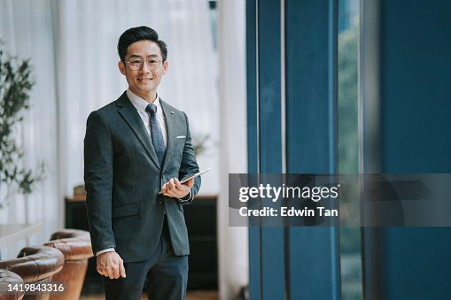 会議室の窓前に立って笑顔でカメラを見つめるアジア系中国人ビジネスマン 会議室の窓前に立って笑顔でカメラを見つめるアジア系中国人ビジネスマン
