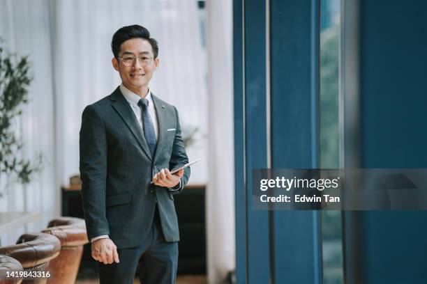 asian chinese businessman looking at camera smiling standing in front of window in conference room - chinese people posing for camera stockfoto's en -beelden