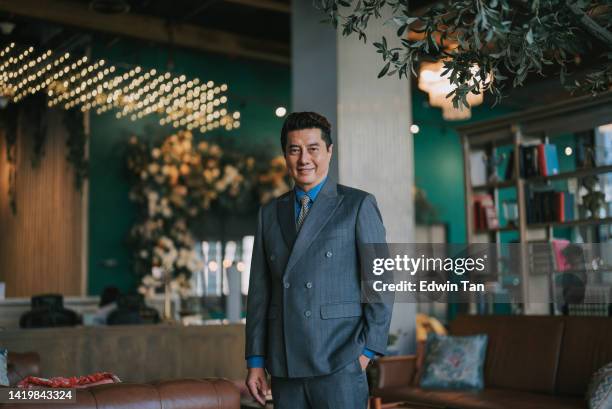 portrait asian chinese successful businessman looking at camera smiling standing at luxury hotel lobby - administratief directeur stockfoto's en -beelden