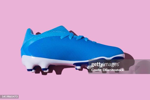 blue soccer boot on pink background. concept of football, world cup, sport, qatar, sports shoes and women's soccer. - football boot stockfoto's en -beelden