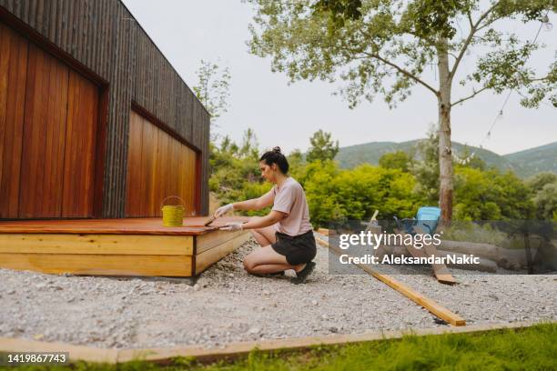 junge frau, die ein holzdeck vor dem haus malt - timber deck stock-fotos und bilder