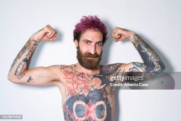 man with tattoos and pink hair smiling while making the power gesture on a white background and looking at the camera - pink hair stock pictures, royalty-free photos & images