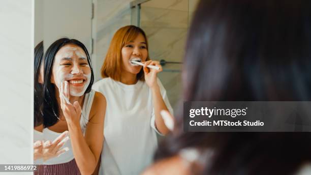 junges asiatisches lgbtq-paar mädchen im badezimmer. glückliche damen haben spaß beim zähneputzen und gesichtsschaumreinigung gesicht vor dem spiegel zusammen in der toilette zu hause. - bad date stock-fotos und bilder