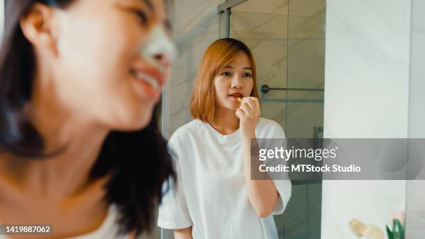 young beautiful asian lgbtq couple ladies in bathroom. happy girls having fun use nose mask cream and put lipstick on lips in lavatory at home. - pore strip stock pictures, royalty-free photos & images