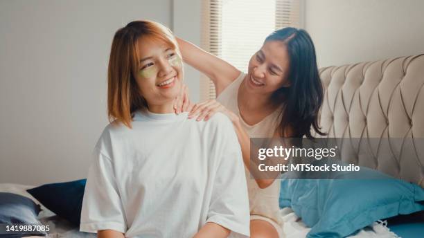 young beautiful asia lesbian lgbt ladies in bedroom. happy girls use daily serum eyes mask on face sit on bed and girlfriends smiling taking care massage shoulder. - girlfriend massage stock pictures, royalty-free photos & images