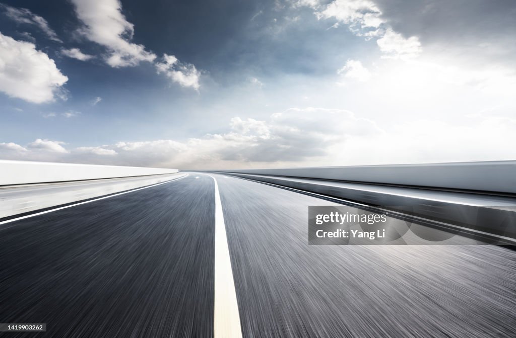 Low and wide angle view of asphalt road with blurred motion in shine day