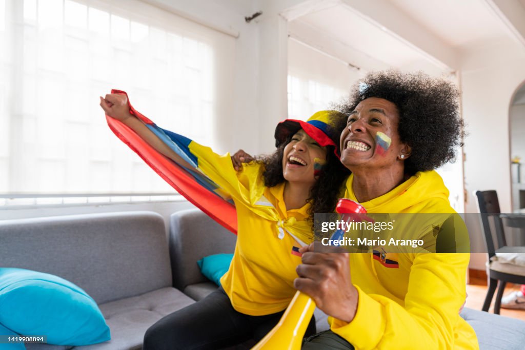 Un par de amigos afro que son fanáticos de la selección ecuatoriana de fútbol se preparan para el partido en su casa vestidos con las camisetas del equipo de fútbol