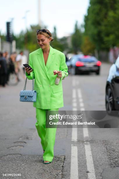 Guest wears black sunglasses, gold earrings, a neon green oversized linen blazer jacket, matching neon green linen suit pants, a blue grained matte...