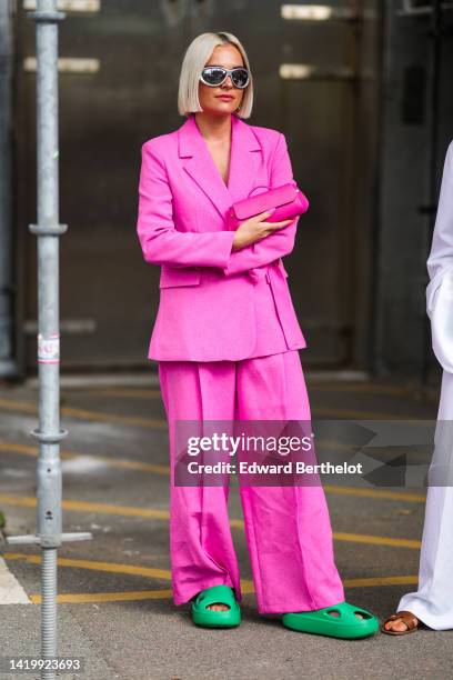 Guest wears silver earrings, a neon pink blazer jacket, matching neon pink large suit pants, a neon pink shiny leather east-west handbag, green...