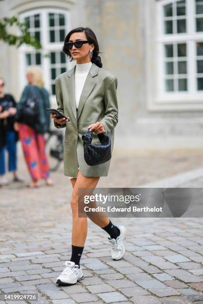 Guest wears black sunglasses, a white pearls pendant earring, a white ribbed high neck / short jumpsuit, a khaki shiny varnished fabric blazer...