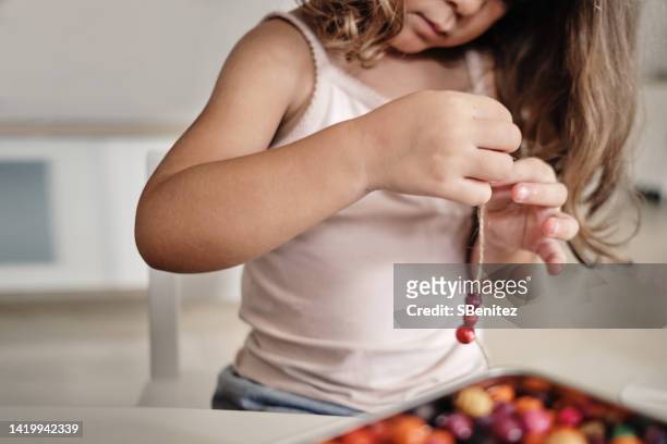 girl making bracelet while sitting on chair at home - bead string stock pictures, royalty-free photos & images