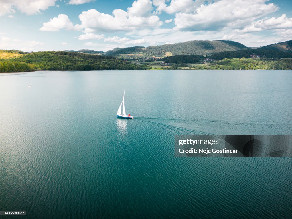 Sailboat sailing alone in light wind on a large lake at sunset