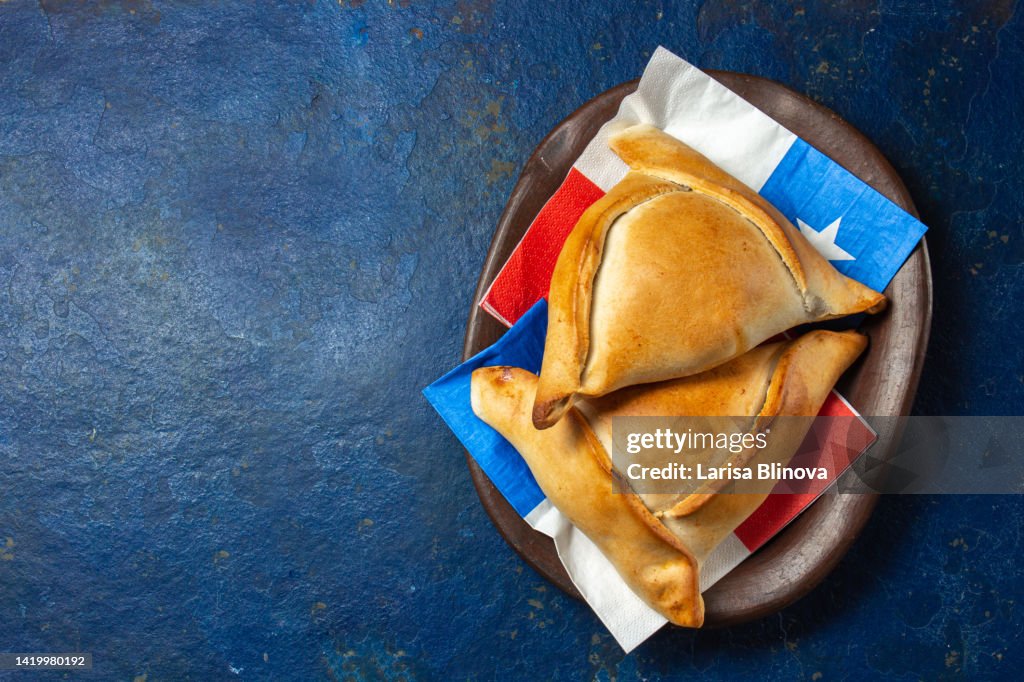 Chilen typical baked empanadas for independence day party on clay plate with chilean festive symbols.