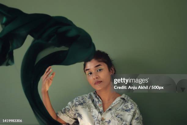 portrait of woman holding green scarf in air against wall - redactioneel stockfoto's en -beelden