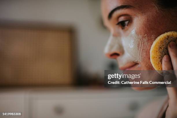 close-up of a woman removing a face mask with a small sponge - body scrub bildbanksfoton och bilder