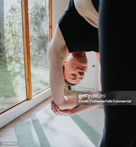 a woman performs a roll-down stretching exercise on a mat - kromme stock-fotos und bilder