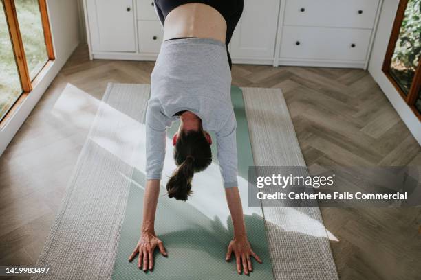 a woman performs the downwards dog yoga / pilates position on a exercise mat - upside down stock pictures, royalty-free photos & images