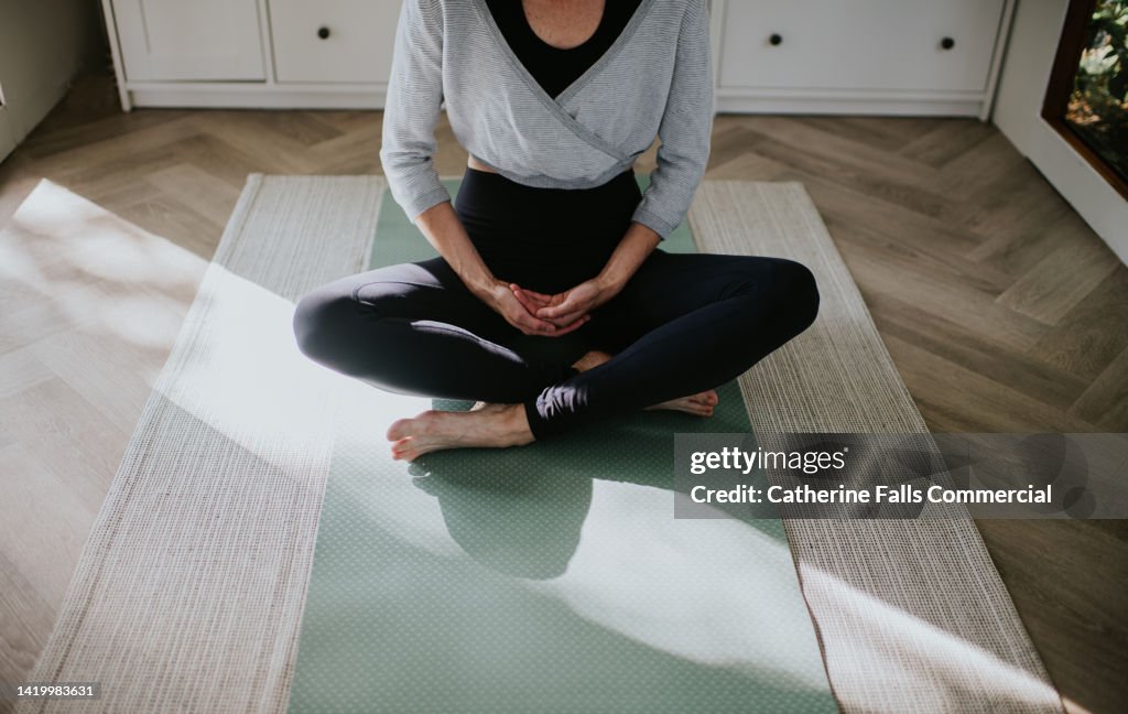 A woman practices yoga / pilates, sitting cross-legged on the ground on her exercise mat.