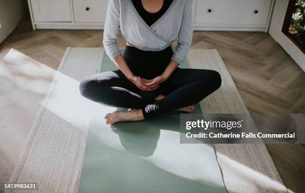 a woman practices yoga / pilates, sitting cross-legged on the ground on her exercise mat. - self discipline imagens e fotografias de stock