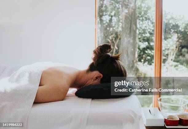 a relaxed woman rests her head into the face port on a massage table, ready for her treatment - back pain bed stock pictures, royalty-free photos & images