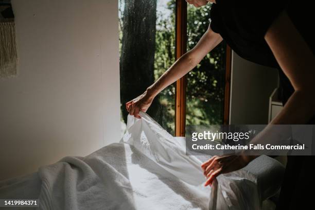 a beauty therapist makes up a massage table with clean sheets and towels - massage table imagens e fotografias de stock