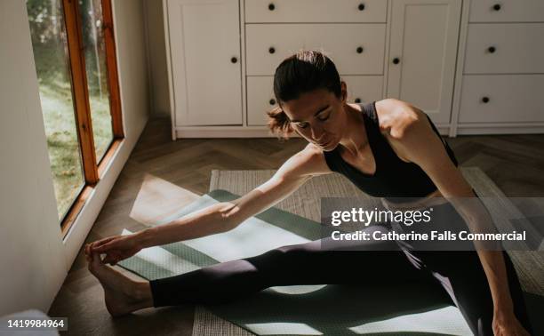 a woman stretches in a sun dappled room, reaching and grabbing her toes - calf human leg stock pictures, royalty-free photos & images