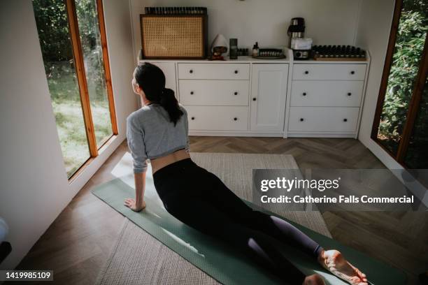 a woman stretches her lower back in the cobra pilates / yoga position - push up knee photos et images de collection
