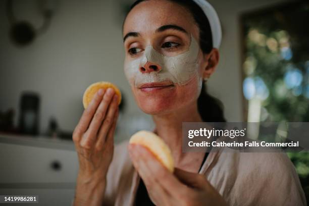 a woman removes a clay face mask with two, small round sponges - blackheads photos et images de collection