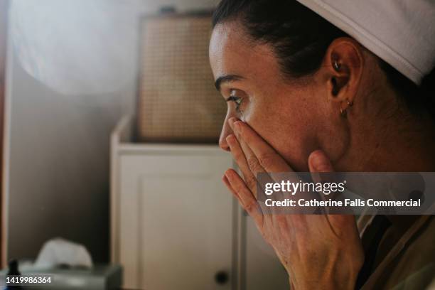 a woman pats beauty products around her eyes and cheeks - adult in mirror stock-fotos und bilder