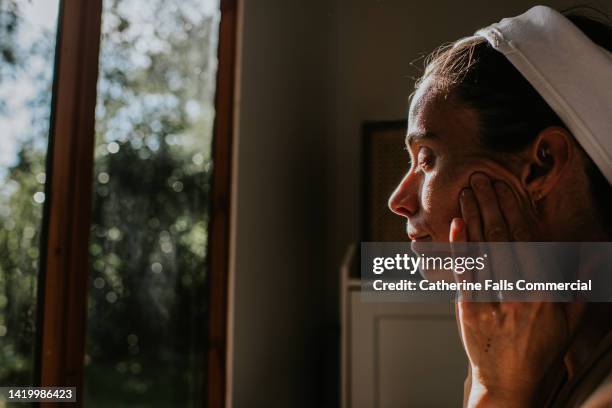 a woman rubs oil into her face - huile de massage photos et images de collection