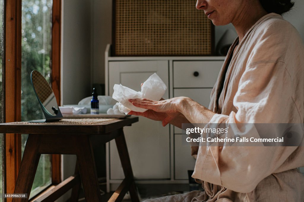 A woman wipes excess beauty product onto a single-use tissue