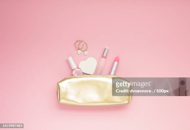 directly above shot of golden female purse with cosmetics on pink background - purses and body care stock pictures, royalty-free photos & images