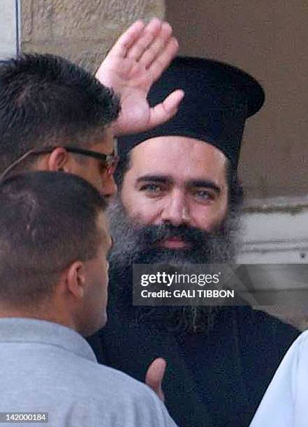 Arab Israeli Greek Orthodox archimandrite Theodosios Hanna waves to the press on his way out of the Jerusalem police station 22 August 2002, escorted...